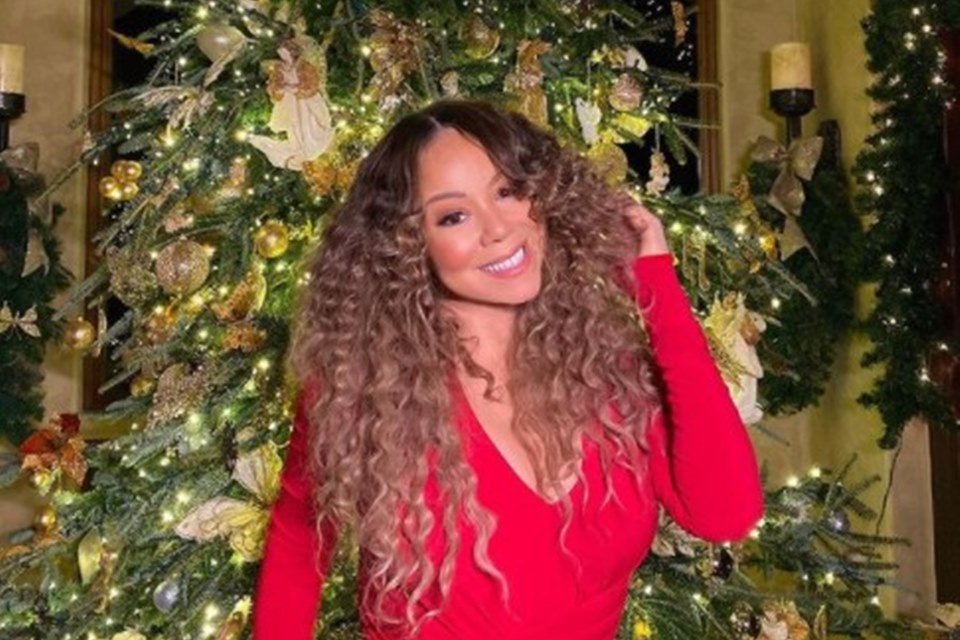 Mulher com cabelo cacheado e vestido vermelho em frente a árvore de Natal