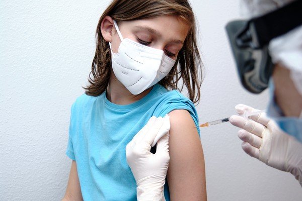 Child sits while someone injects a syringe into his arm - Metropolis
