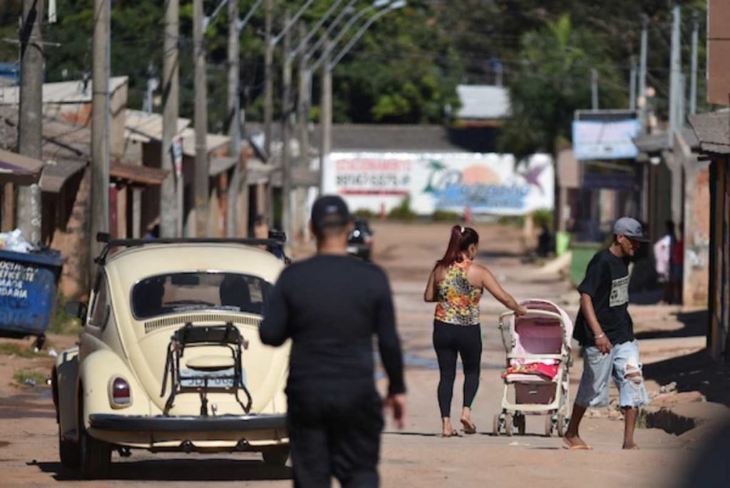 três pessoas em uma longa rua, cada uma em uma parte desta via. mais para trás uma mulher com um carrinho rosa no meio da pista e, ao lado, um homem saindo de perto da mulher com o carrinho