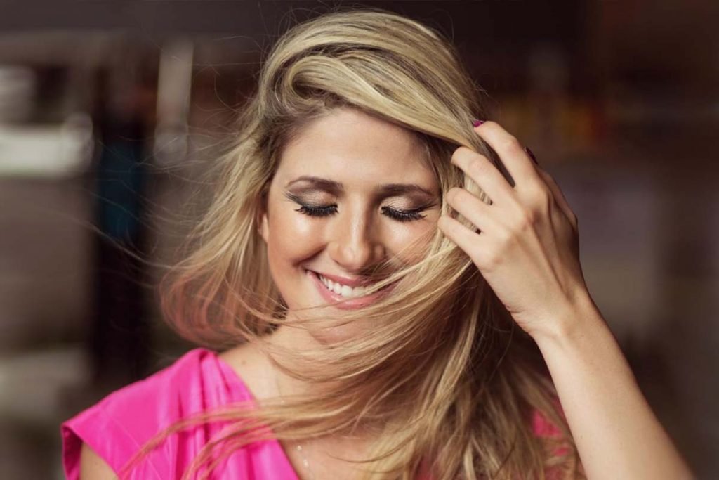 Foto de Dani Calabresa. Ela está sorrindo, com a mão no cabelo loiro, e de blusa rosa - Metrópoles