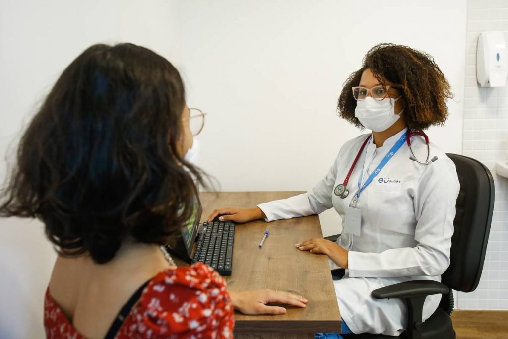 Fotografia colorida. Mulher é atendida por médica em consultório