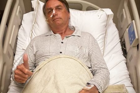 Bolsonaro em cama de hospital com sonda nasogástrica e fazendo sinal de joinha