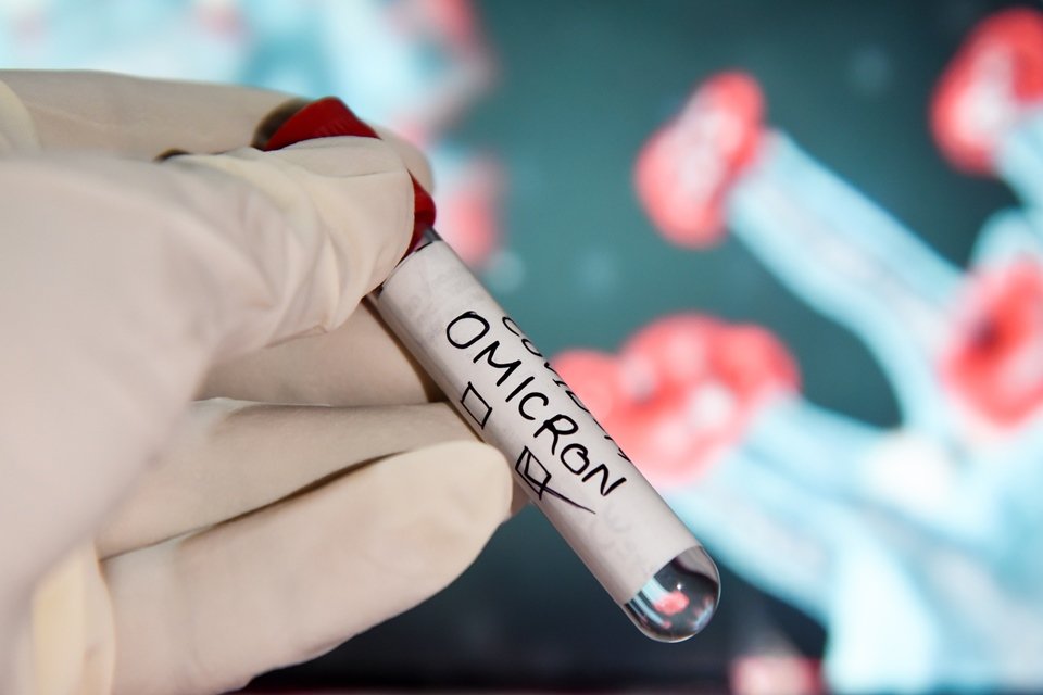 Imagem colorida: mão de cientista com luva segura pote com amostra de variante Ômicron - MKetrópoles