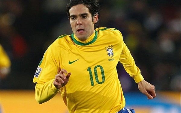 Na imagem colorida, um homem está centralizado no centro. Ele usa camisa do Brasil e está em um campo de futebol