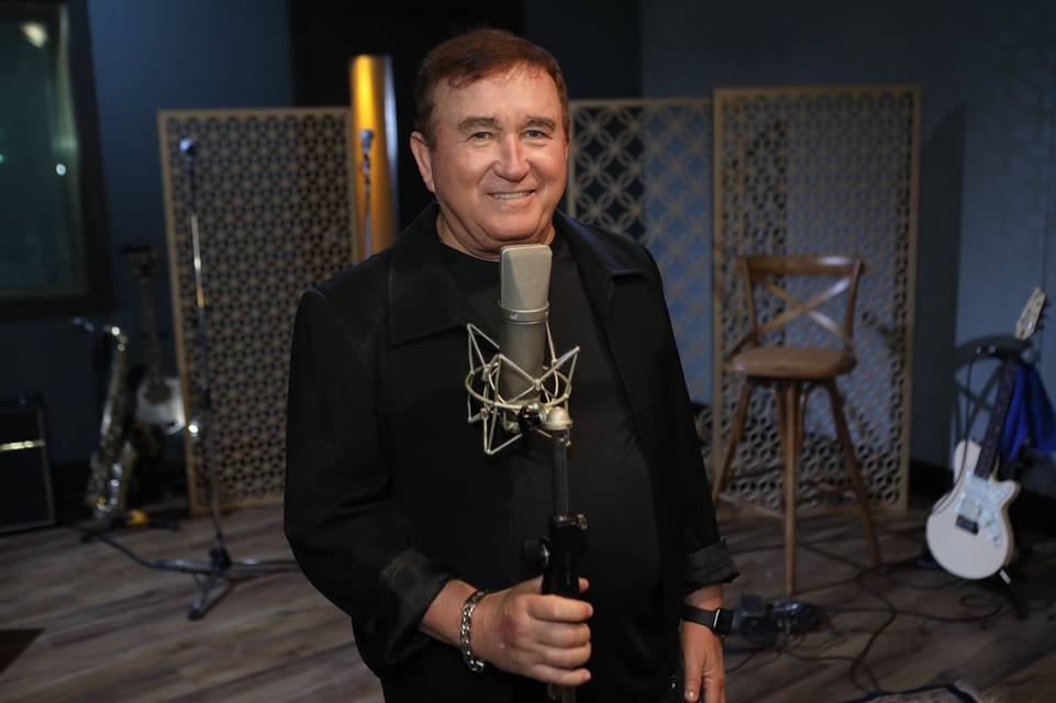 Foto colorida do cantor Amado Batista. Ele usa um blazer preto e segura um microfone. Está sorrindo - Metrópoles