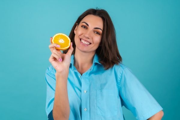 Fotografia colorida de mulher sorrindo e segurando uma laranja