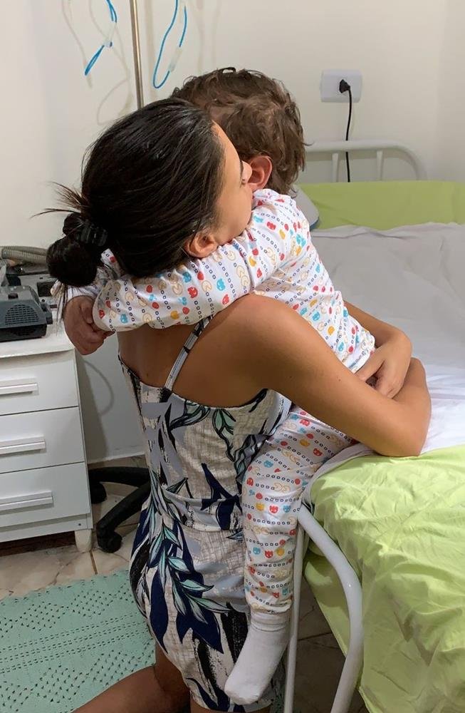 Karita Lorraine abraça Arthur Miranda, em casa, onde menino faz tratamento para estimular o cérebro, em Goiânia, Goiás
