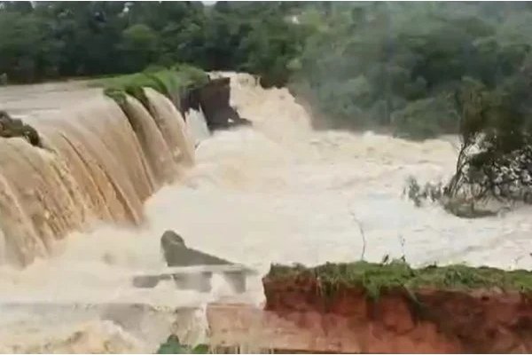 Na imagem colorida, uma barragem está estremamente cheia e água vaza pelos lados