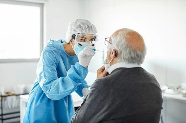 In the color image, a person in blue puts a cotton swab into the mouth of a seated elderly man.