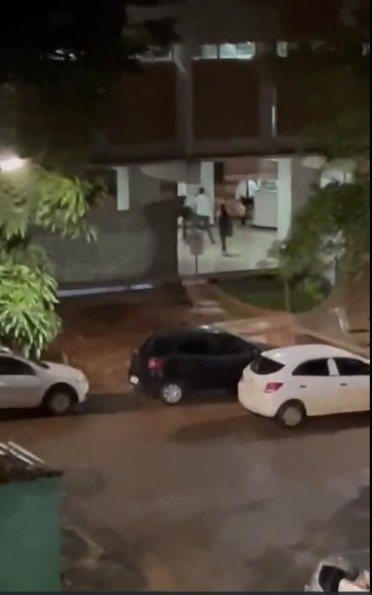 Carros estacionados, homens agarrados no pilotis de bloco residencial