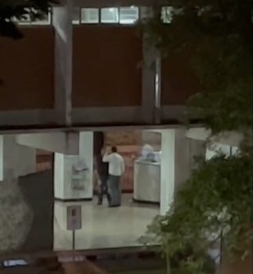 Três pessoas, na área comum de um prédio, em posição de briga