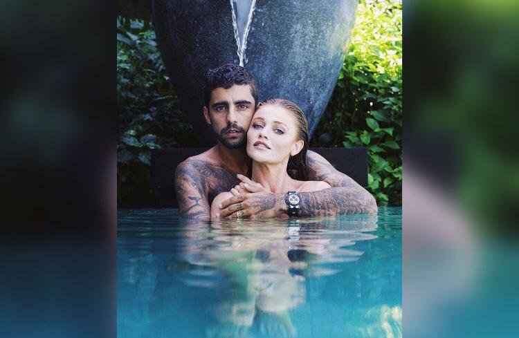 Na imagem colorida, um homem e uma mulher estão posicionados no centro. Eles estão um ao lado do outro e olham seriamente para a camera