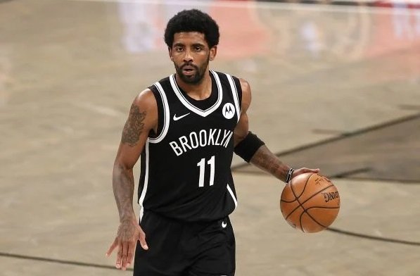 Na imagem colorida, um homem está posicionado no centro. Ele usa uniforme verde e segura uma bola de basquete nas mãos