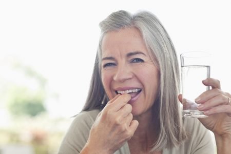 Mulher toma medicamento enquanto segura copo de água