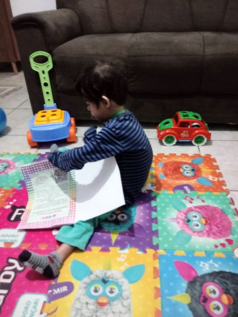 Menino sentado em tapete colorido, segurando papéis