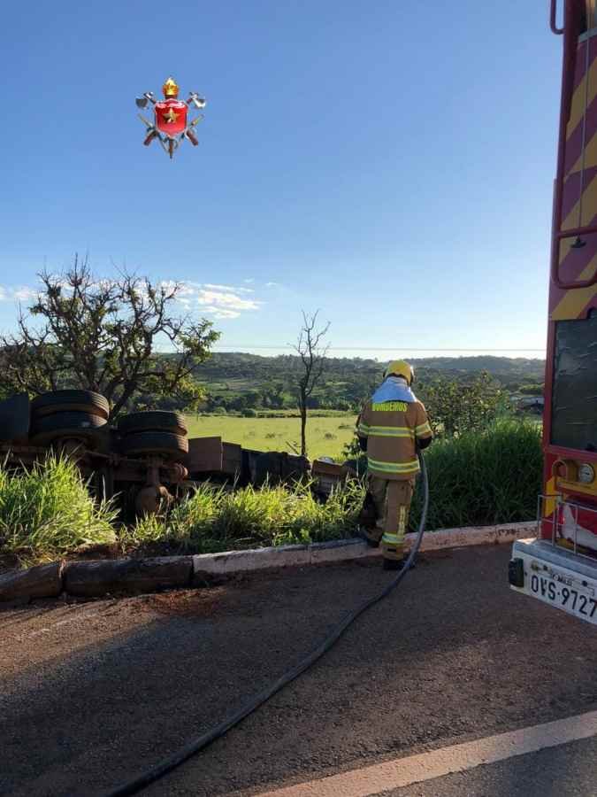 caminhão tombado fora da pista, bombeiro (vestido de amarelo) com mangueira a fim de evitar incêndios