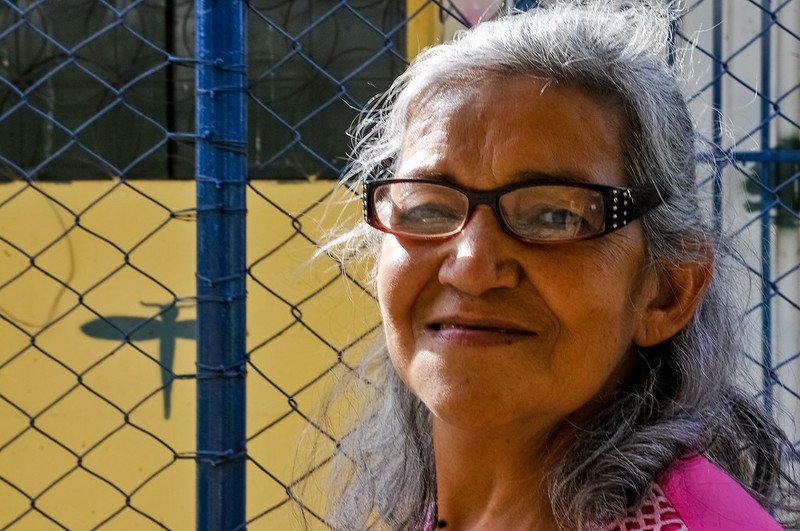 Mulher de óculos e cabelos brancos sorrindo em frente a grade