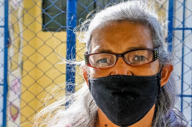 Mulher de óculos, máscara preta e cabelos brancos em frente a grade