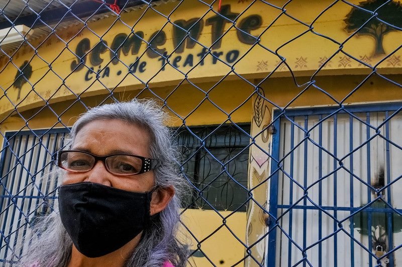 Mulher de óculos, máscara e cabelos brancos em frente a grade