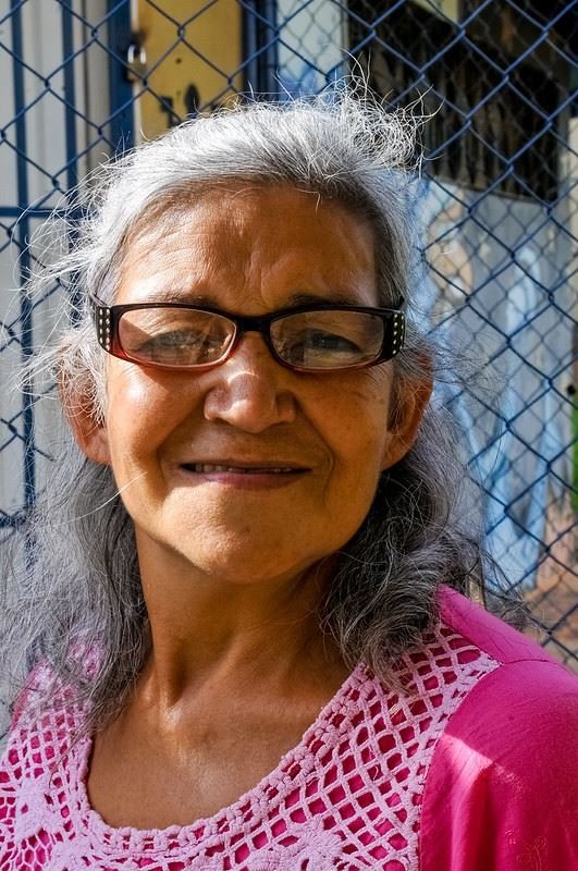 Mulher de óculos e cabelos brancos sorrindo em frente a grade
