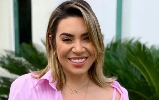 Na imagem colorida, uma mulher está posicionada no centro. Ela tem cabelos curtos e loiros, olhos castanhos e sorri para a câmera