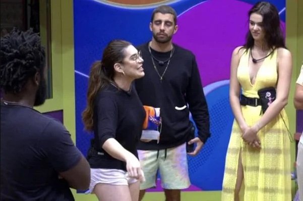Na imagem colorida, uma mulher está posicionada no centro. Ela tem cabelos curtos e loiros, olhos castanhos e sorri para a câmera