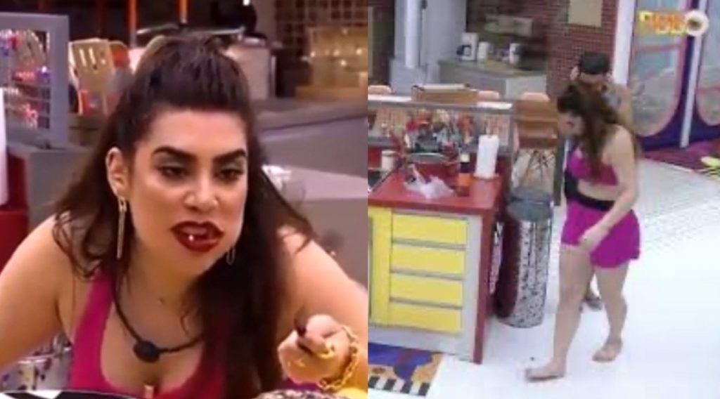 Na imagem colorida, uma mulher está posicionada no centro. Ela tem cabelos curtos e loiros, olhos castanhos e está com comida na boca enquanto fala