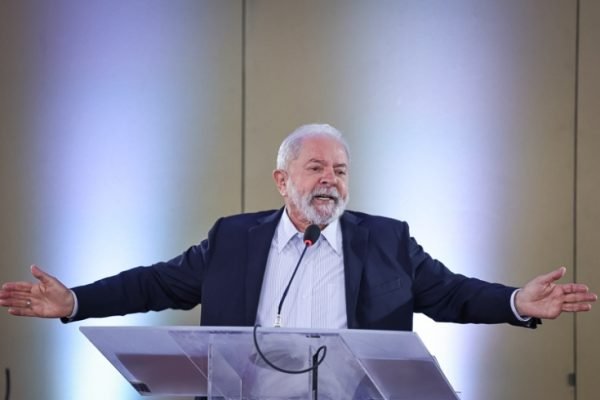 Lula em coletiva de imprensa discursando. Ele está em frente a um púlpito e fala ao microfone, de braços abertos - Metrópoles