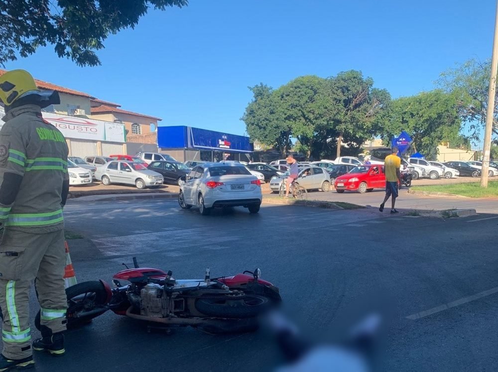 Moto vermelha deitada no chão e corpo de pessoa coberto por pano em asfalto