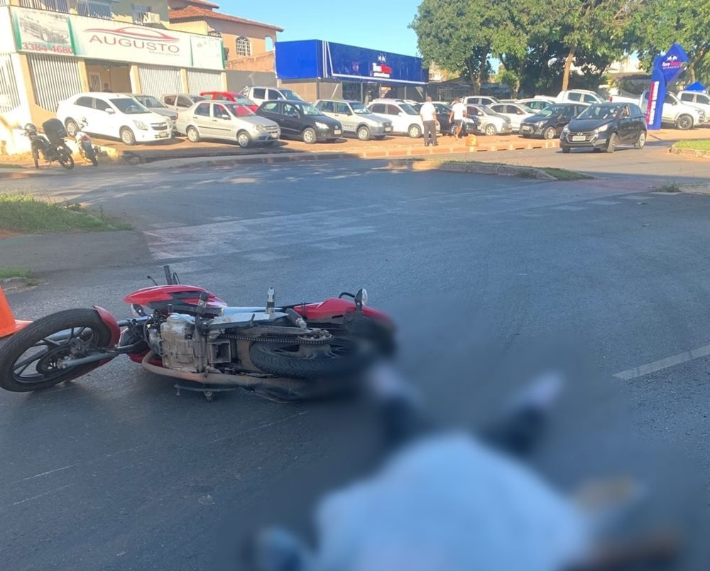Moto vermelha deitada no chão e corpo de pessoa coberto por pano em asfalto