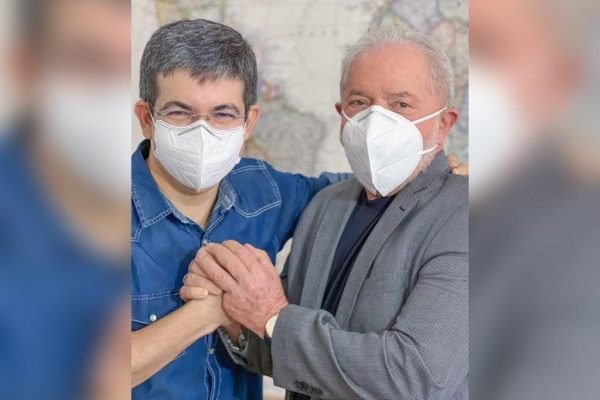 Na imagem, o senador Randolfe Rodrigues (Rede) e o ex-presidente Lula (PT) posam para foto de mãos dadas em sinal de união. Ambos usam máscara e sorriem - Metrópoles