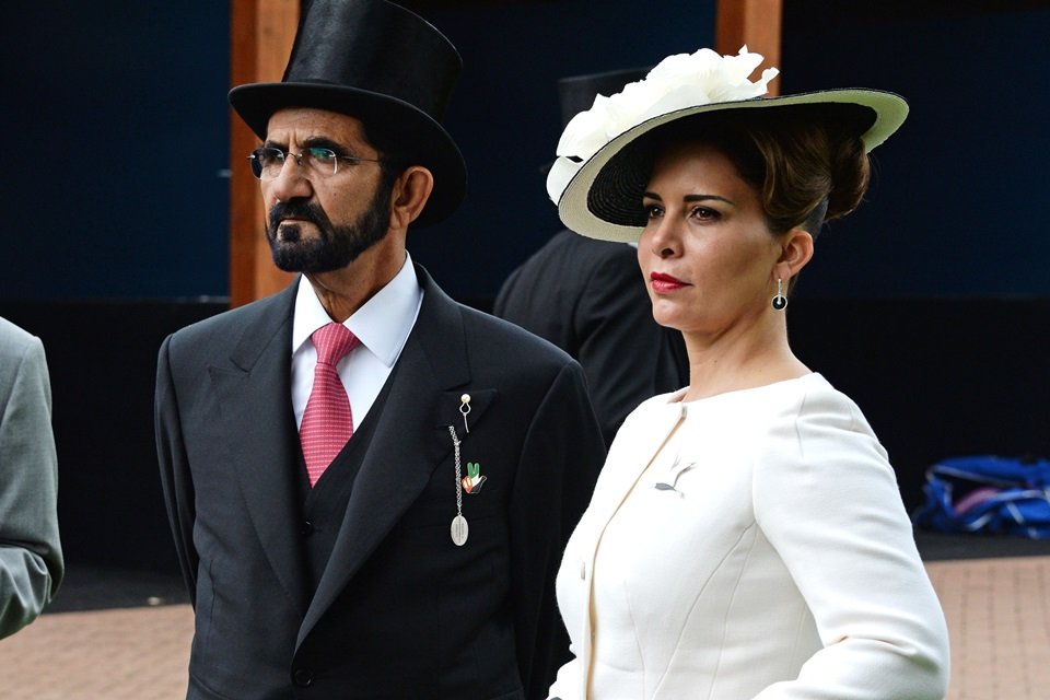 Homem de óculos e com chapéu ao lado de mulher com chapéu e vestido branco