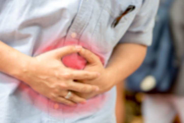 Na imagem colorida, uma pessoa está posicionada no centro. Ela usa camiseta clara e está com as mãos sobre a barriga