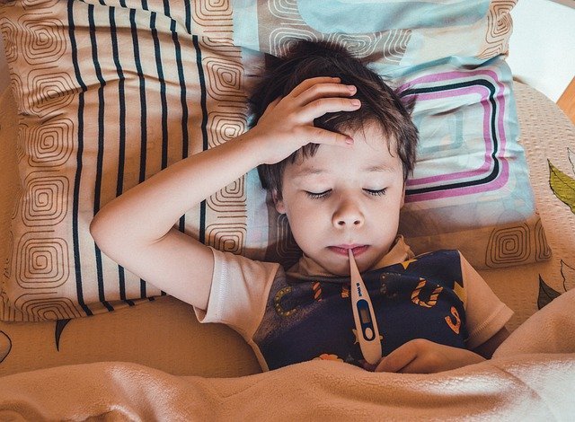 Fotografia colorida de menino com febre medindo a temperatura