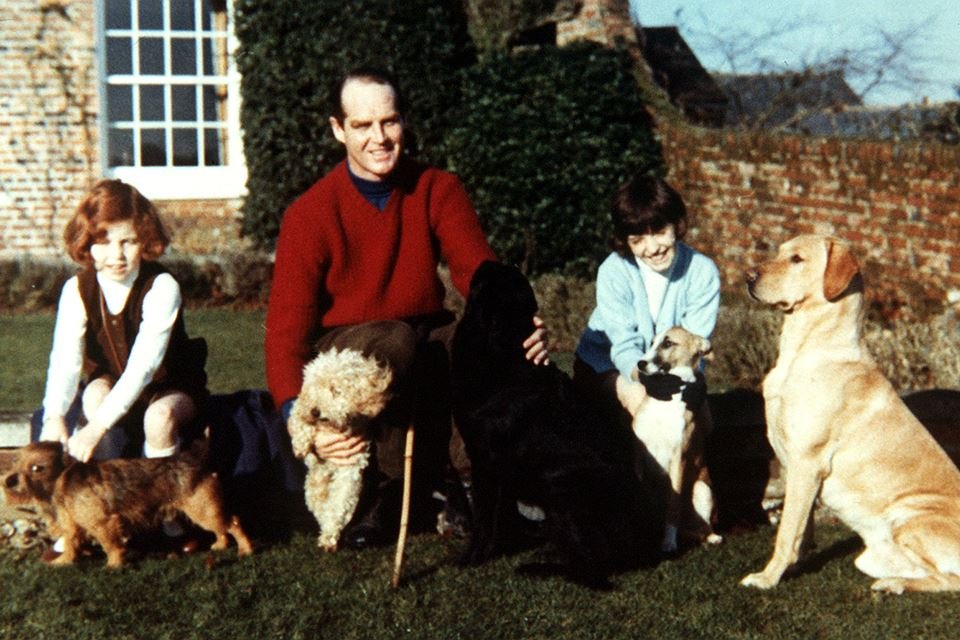 Homem ao lado de duas meninas e cachorros. Eles estão em um jardim