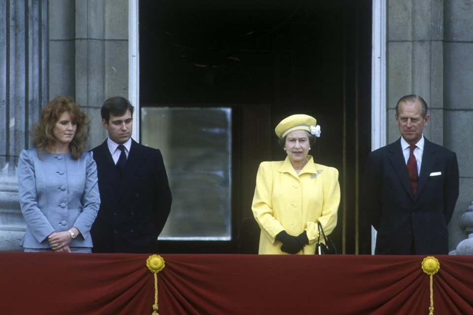 Mulher de roupa azul ao lado de homem de terno. Mulher de trajes amarelo ao lado de homem de terno. O quarteto está em uma varanda
