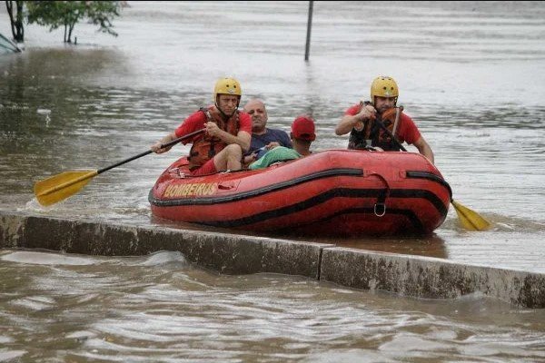 Na imagem colorida, um barco dos bombeiros está resgatando um homem de uma área inundada.