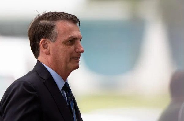 Bolsonaro aparece de perfil, usando terno e gravata, sem máscara, em algum lugar do Palácio da Alvorada, sorrindo - Metrópoles
