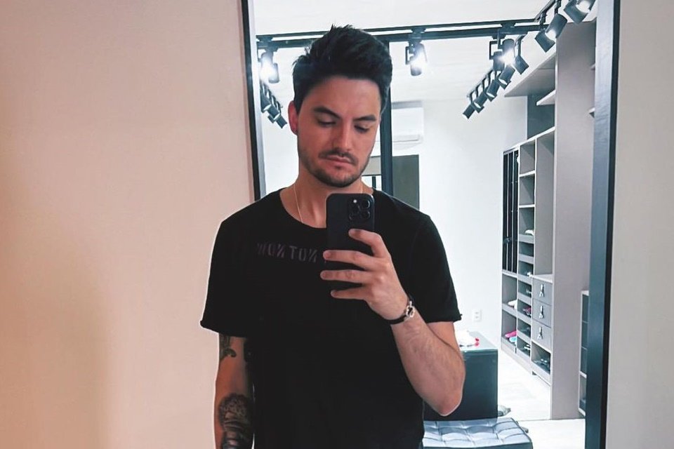 Felipe Neto wears a black t-shirt and takes a photo when he looks at his cell phone-Metropolis