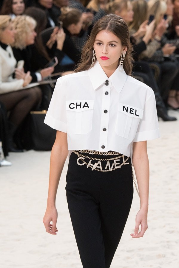 Modelo Kaia Gerber em desfile da Chanel com camisa branca e calça preta da marca