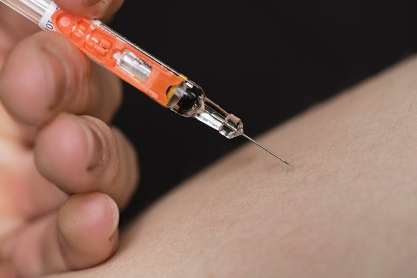 In the color image, a needle is under the clean skin.  The syringe is orange.
