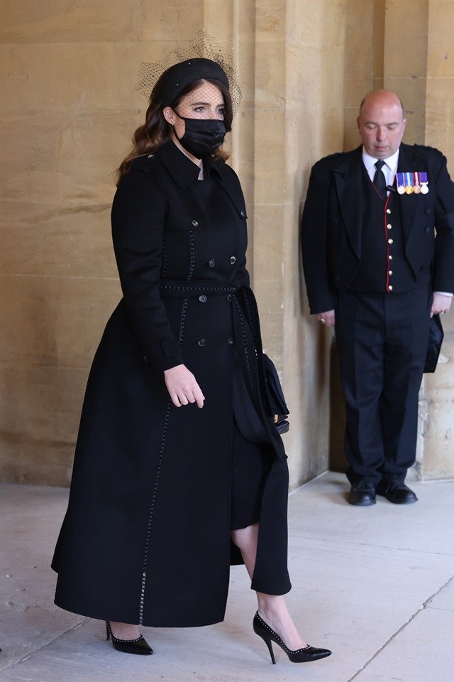 Mulher de casaco e máscara preta. Ao fundo, soldado com trajes militares
