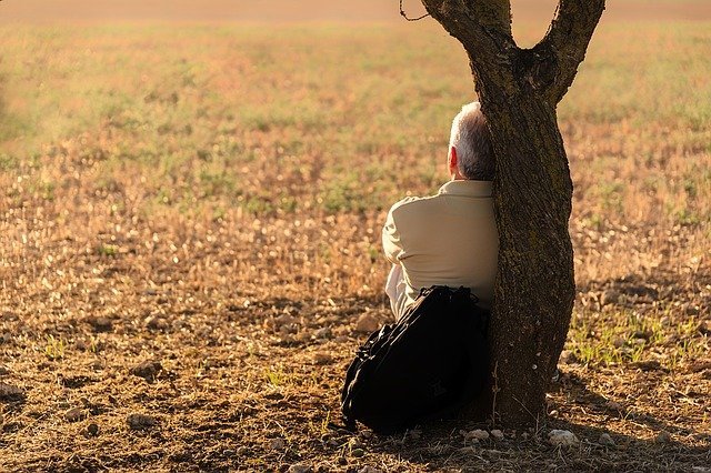 Colored photograph of an elderly man leaning against a tree