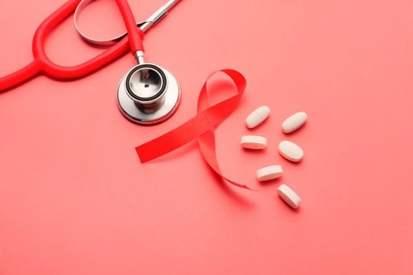 Imagem colorida de fita vermelha símbolo do HIV, pílulas de remédio e estetoscópio - Metrópoles