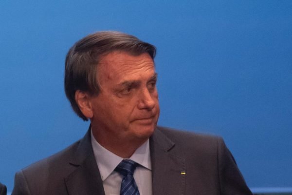 Bolsonaro em evento no Planalto de ações ao crédito. Ele olha para o lado, sem máscara e sob fundo azul, preocupado - Metrópoles