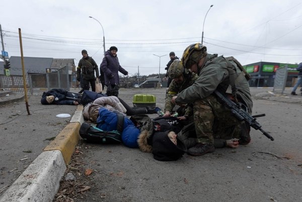 Soldados tentam salvar a vida de civil criado no chão após bombardeio russo.  Ao lado, estirados, estão os corpos de seus familiares mortos - Metrópoles