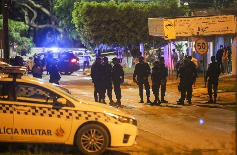 Viatura da polícia militar estacionada e policiais ao fundo, à noite