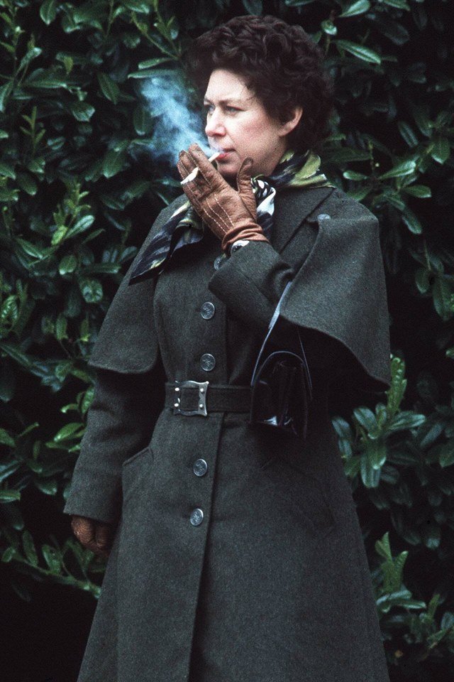 Mulher fumando cigarro. Ela está com um casaco longo