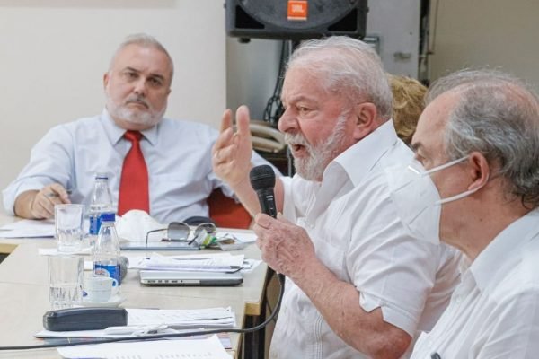 Em foto, aprece ao fundo o senador Jean Paul Prates (PT), o ex-presidente Lula (PT) e o ex-senador Aloísio Mercadante (PT). Lula tem um microfone na mão e discursa. Todos usam camisas sociais, e apenas Mercadante está de máscara - Metrópoles