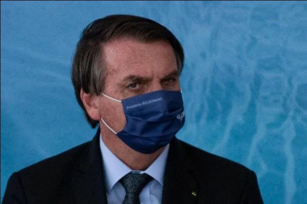Bolsonaro em evento no palácio do Planalto.  Ele usa terno e, camiseta clara máscara na cor azul e olha para a câmera - Metrópoles